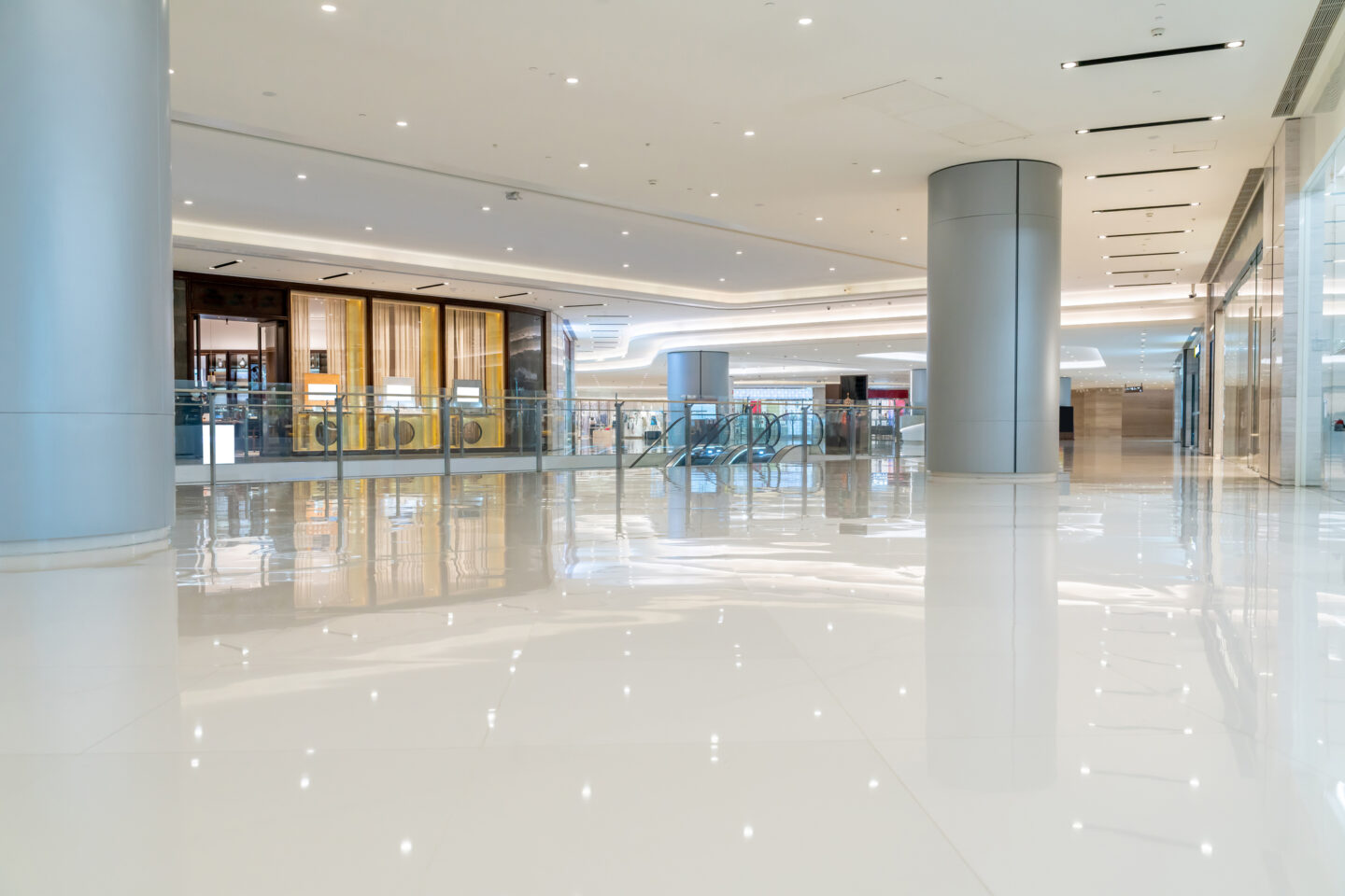 Spacious, empty shopping mall interior with glossy white floors, large columns, glass railings, escalators, and storefronts in the background—similar to environments where pest control for hospitals and medical facilities is crucial.