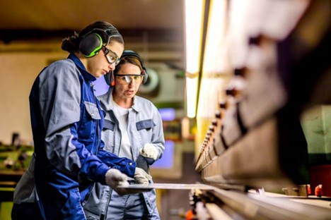 Women in safety gear operating a press brake machine in a manufacturing facility.
